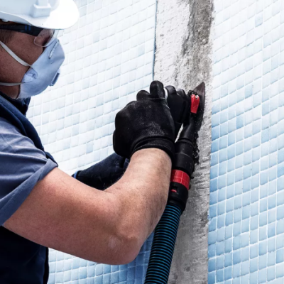 Homem a remover azulejos azuis de parede com ferramenta especializada.