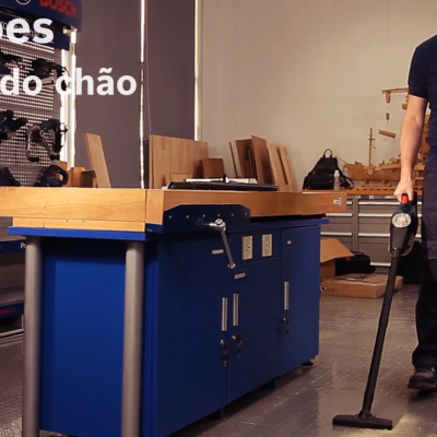 Homem numa oficina usando aspirador de chão ao lado de móvel de trabalho azul e texto Aplicações Aspiração do chão