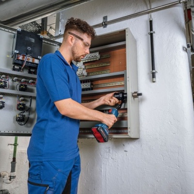 Homem com furadeira elétrica a trabalhar num quadro elétrico aberto na parede