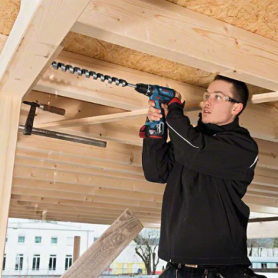 Homem a usar ferramenta elétrica para aparafusar vigas de madeira clara no teto de uma construção