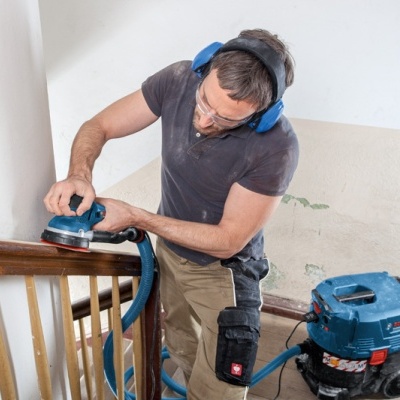 Homem a lixar corrimão de madeira com lixadora elétrica azul