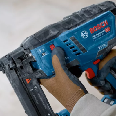 Máquina de ferrar Bosch profissional azul e preta com texto legível sendo segurada por mãos com luvas