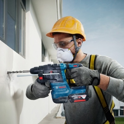 Martelo perfurador Bosch azul em uso por trabalhador com equipamento de proteção, perfurando parede branca externa