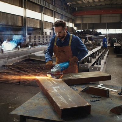Homem a usar rebarbadora azul em oficina industrial com faíscas no trabalho de metal