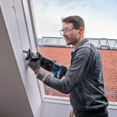 Homem a usar furadeira em construção com telhado vermelho ao fundo