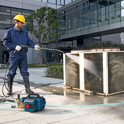 Homem a limpar unidade de ar condicionado ao ar livre com máquina de alta pressão