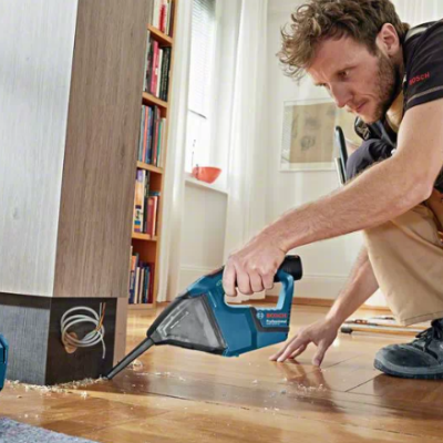 aspirador de pó portátil azul a ser usado por homem num chão de madeira próximo de móvel