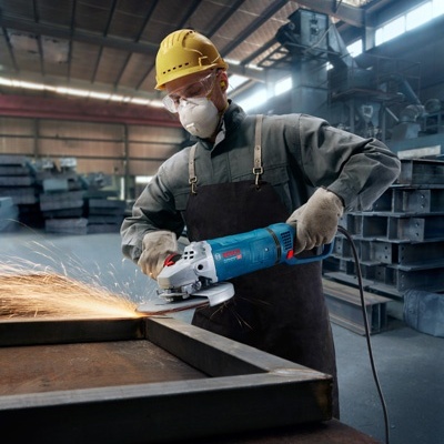 Pessoa com equipamento de proteção usando esmerilhadora em máquina na fábrica