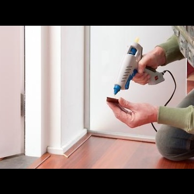 Pessoa a usar pistola de cola quente para colar pedaço de madeira no chão