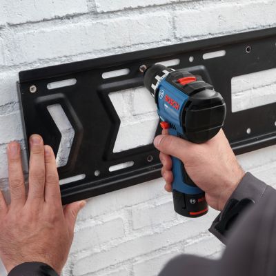 Parafusadeira Bosch azul e preto a fixar suporte metálico preto numa parede branca de tijolos