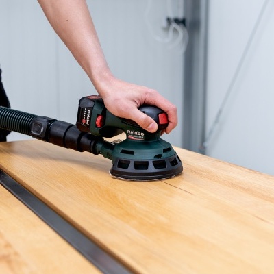 Lixadeira eléctrica verde e preta numa superfície de madeira clara