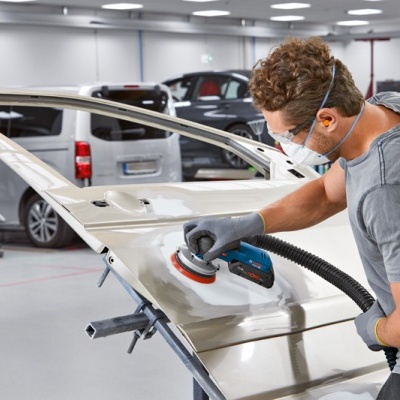 Homem a lixar uma porta de carro branca numa oficina automóvel