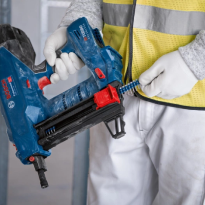 Pessoa com colete amarelo e luvas segurando pistola de pregos azul e preta BOSCH