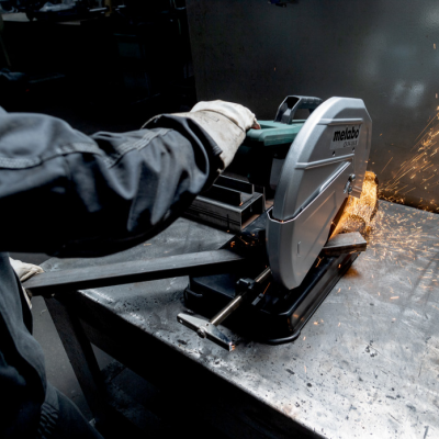 Serra de corte Metabo a cortar metal com faíscas numa bancada, trabalhador com luva