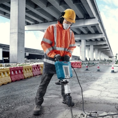 Trabalhador a operar martelo pneumático azul em obra sob uma ponte