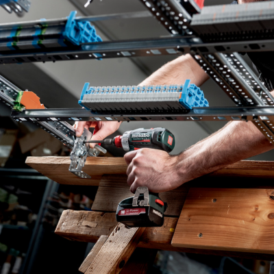 Pessoa a usar furadeira elétrica para fixar estrutura metálica numa oficina