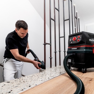 Homem usando aspirador metabo preto e vermelho no corredor com chão de madeira