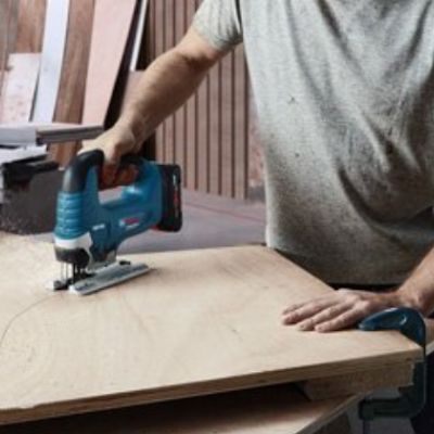 Pessoa usando serra tico-tico azul para cortar chapa de madeira