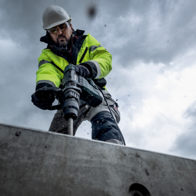 Trabalhador com capacete e casaco amarelo usando furadeira elétrica
