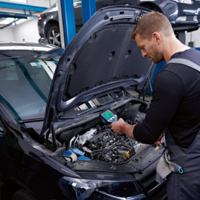 Homem a trabalhar no motor de um carro preto com capot aberto numa oficina.