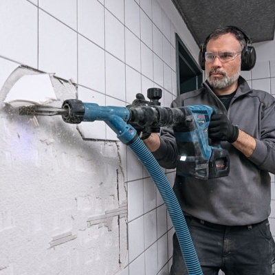Homem a usar martelo perfurador para remover azulejos brancos numa parede interior