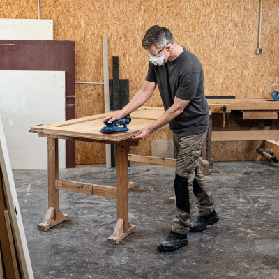Homem a lixar peça de madeira numa oficina