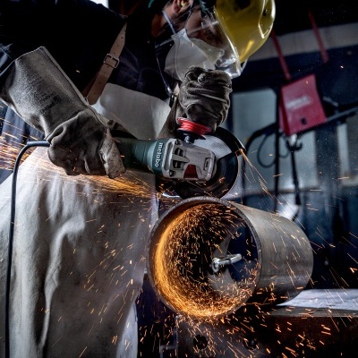 Pessoa a usar esmeril elétrico para cortar tubo metálico com faíscas