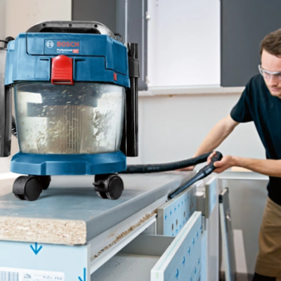 Aspirador Bosch azul com tampa vermelha e transparente sobre mesa, homem a usar ferramenta