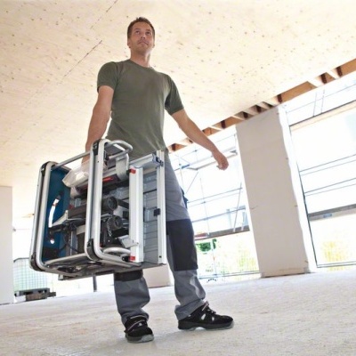 Gerador portátil cinza e preto transportado por homem em interior amplo e bem iluminado