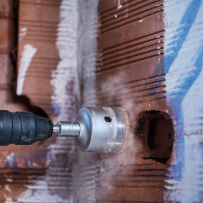 Furadeira com broca circular a perfurar parede de tijolos com reboco.