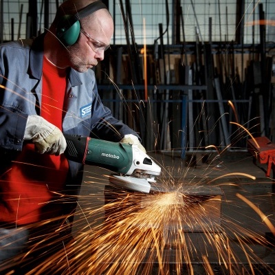 Homem a usar rebarbador e proteção na oficina com faíscas voando