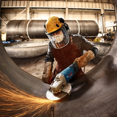 Operário a usar esmerilhadeira Bosch para cortar metal numa fábrica.