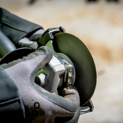 Moedor de ângulo metálico com disco de corte preto sendo segurado por mão com luva cinza