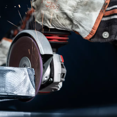 Mãos com luvas a usar rebarbadora elétrica para cortar metal