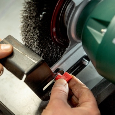 Maquina com escova metálica a limpar peça metálica preta