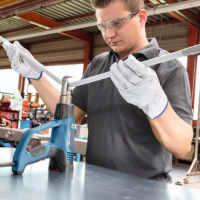 Homem a usar chave de torque numa oficina com pistola de calor