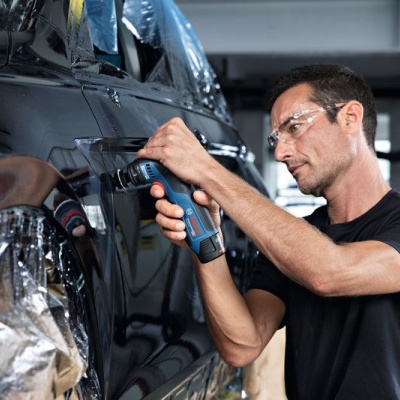 Homem a usar ferramenta elétrica para reparar carro preto numa oficina