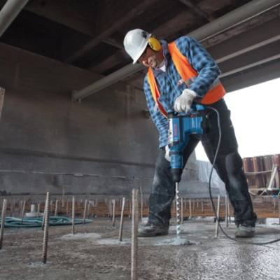 Trabalhador de construção com equipamento de segurança a usar martelo pneumático azul em betão.
