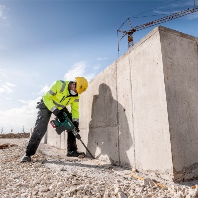 Trabalhador da construção com capacete e colete refletor usando ferramenta elétrica junto a grande estrutura de concreto