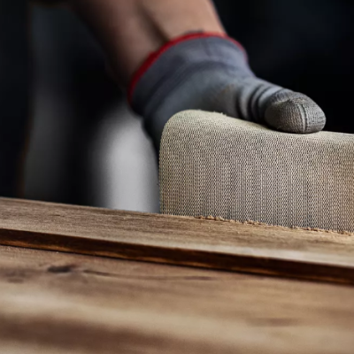 Mão com luva a lixar um pedaço de madeira clara