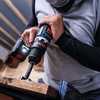 Pessoa a usar furadeira elétrica preta e vermelha para perfurar madeira