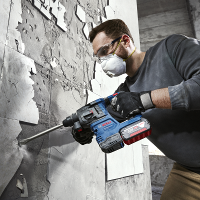 Homem a usar martelo perfurador BOSCH numa parede de azulejos e cimento.