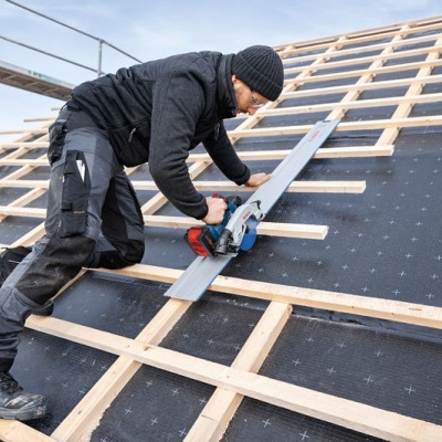 Homem a cortar madeira num telhado com ferramenta elétrica