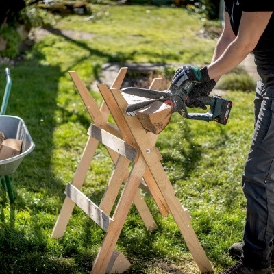 Serra eléctrica a cortar madeira numa bancada de madeira ao ar livre com carrinha de madeira ao lado