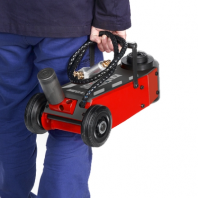 Pessoa segurando macaco hidráulico vermelho com rodas pretas e mangueira