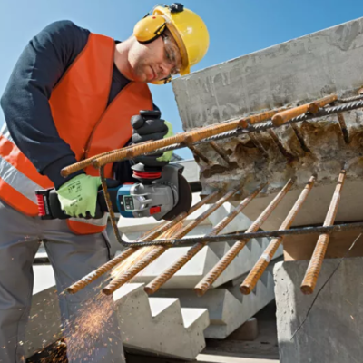 Homem com equipamento de proteção a cortar barras de ferro com rebarbadora numa obra