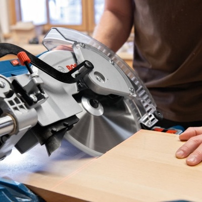 Serra de corte a cortar madeira clara com mão a segurar a peça