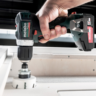 Parafusadeira elétrica preta e verde escuro da Metabo em uso num objeto branco