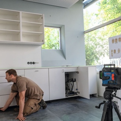 Homem a instalar armários brancos junto a janela grande com tripé e cartaz com diagramas