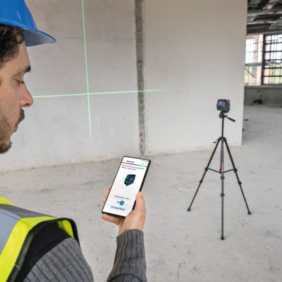 Homem com capacete e colete a usar smartphone para controlar aparelho em tripé numa construção interna